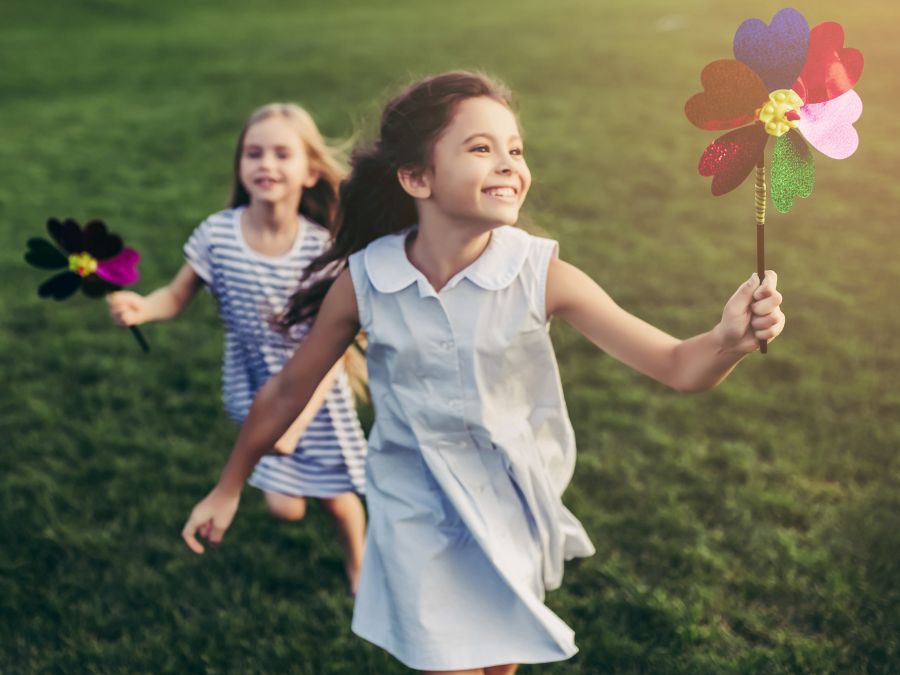 Two young girls running on grass with pinwheels.