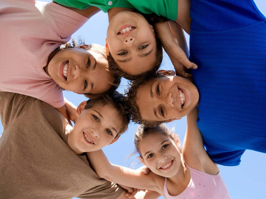Group of 5 kids huddled together smiling.