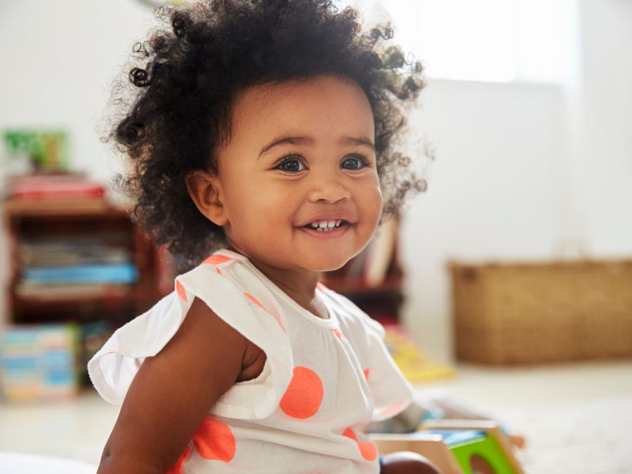 Baby smiling at camera while sitting on the floor.