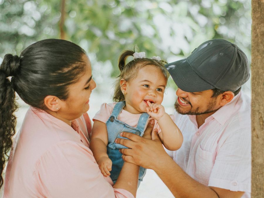 Two parents holding their baby girl who is smiling.