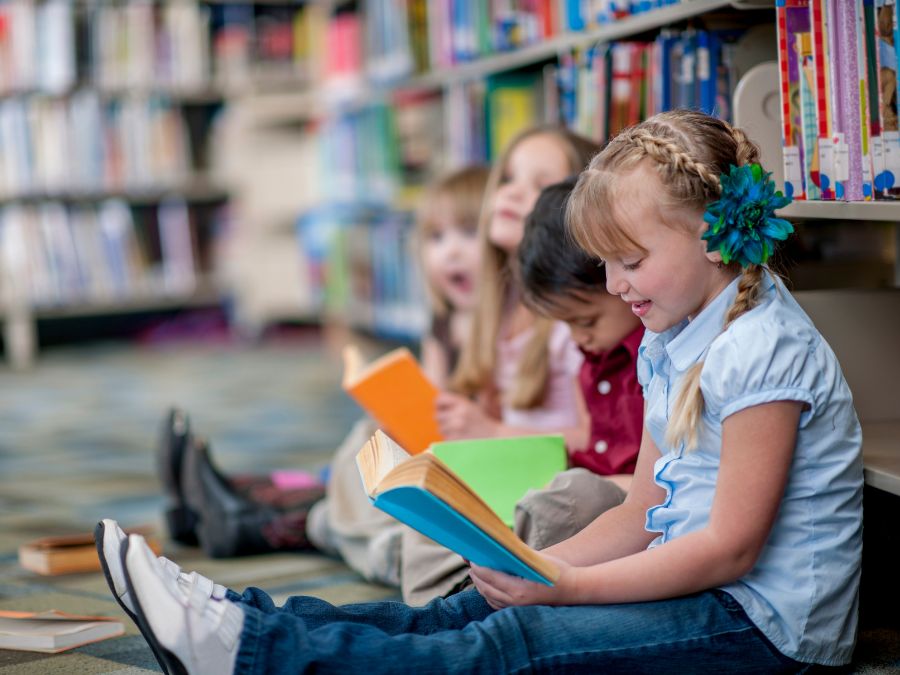 Four children reading books at library.