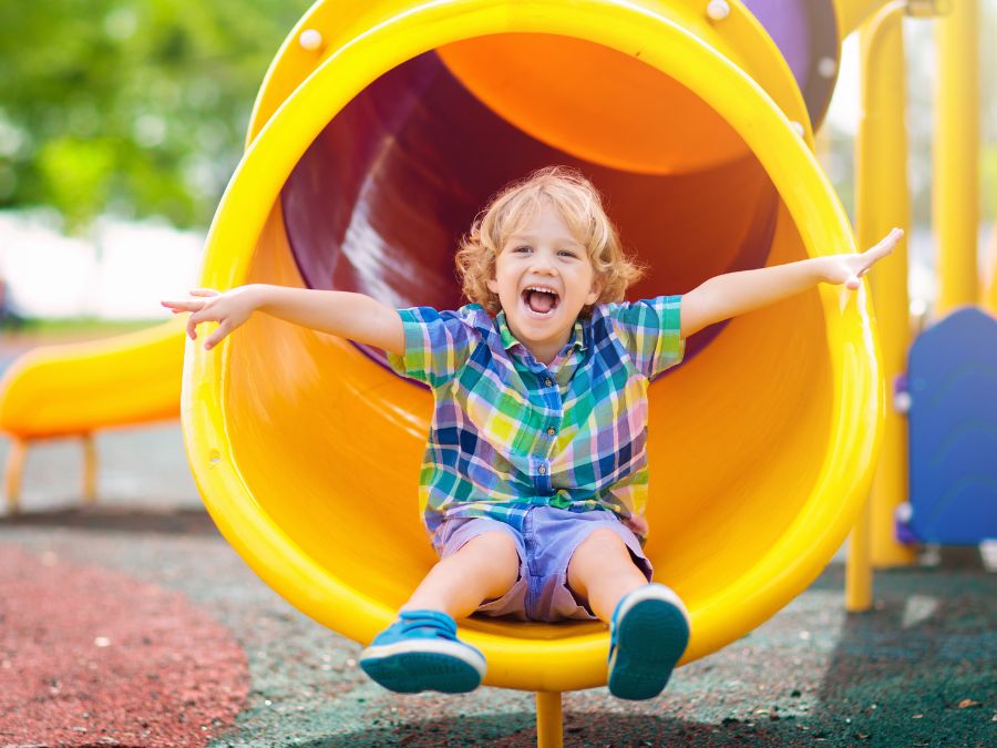Young boy sliding down a yellow tube slide.